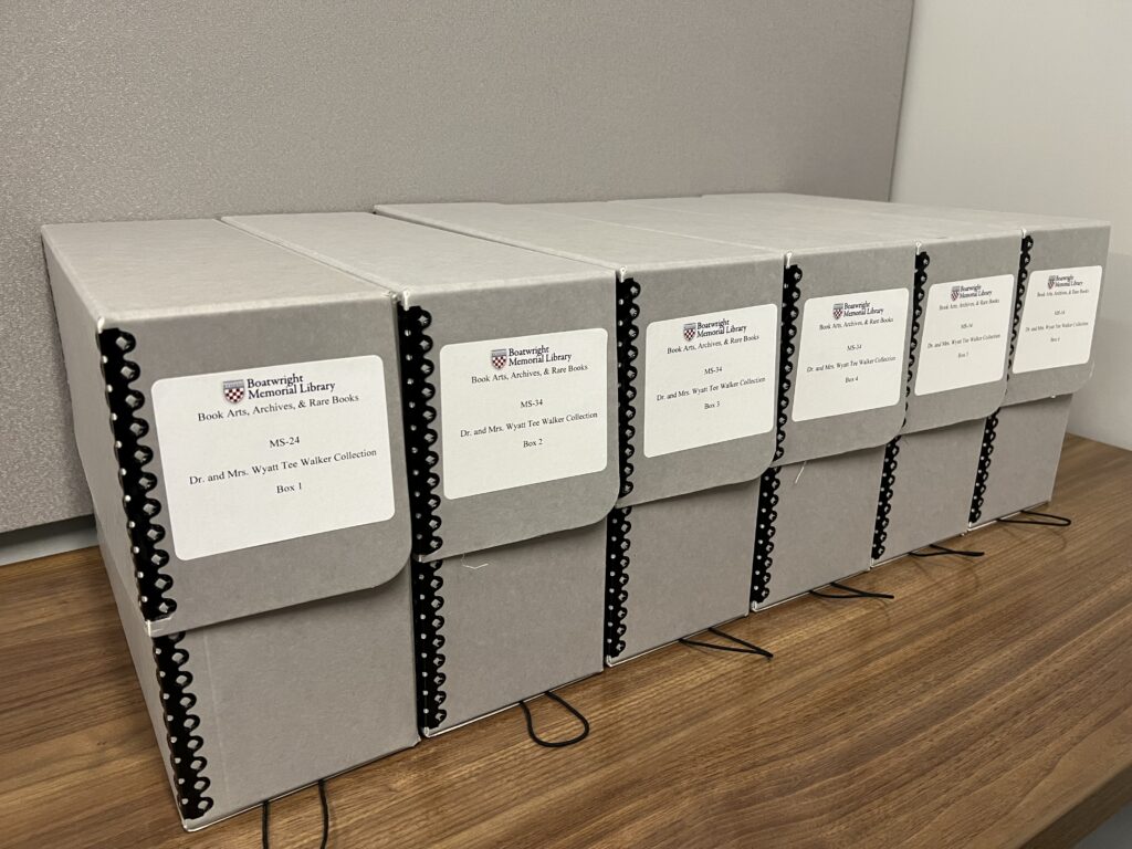 Six grey, legal size, archival boxes sitting in a row on a wooden desk. Each box bears a white label reading "Boatwright Memorial Library Book Arts, Archives, and Rare Books, MS-24 Dr. and Mrs. Wyatt Tee Walker Collection" followed by a box number.